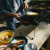 unrecognizable man frying eggs in camping