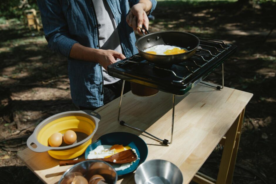 unrecognizable man frying eggs in camping